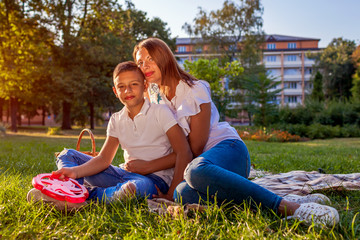 Happy family spending time outdoors sittting on grass in park. Mother with her son hugging and...