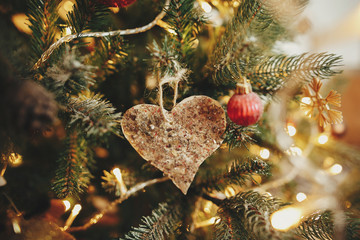 christmas retro heart ornament on beautiful christmas tree with golden lights. handmade vintage toy...