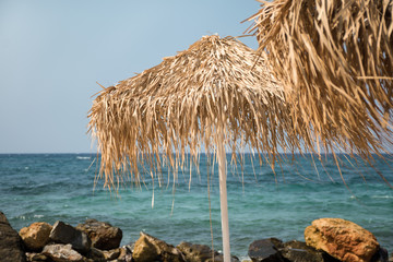 Two tropical parasols with rocks and blue sea in the background, selective focus
