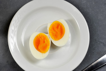Two halves of a hard-boiled chicken egg. The egg lies on a white plate. Gray background. View from...