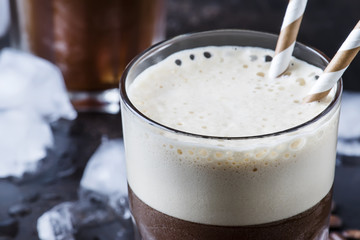 Cold frappe coffee with ice and foam in large glasses on brown background, selective focus