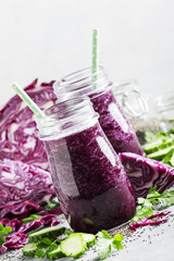 Vegan vegetable smoothie with purple cabbage, cucumber and chia seeds in glass bottles on gray table, selective focus