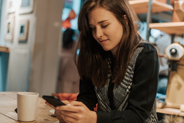 Beautiful young brunette looking at her phone in a coffee shop