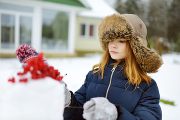 Adorable little girls building a snowman in the backyard. Cute children playing in a snow.
