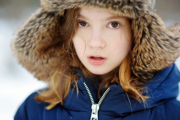 Adorable little girl having fun in beautiful winter park. Cute child playing in a snow.