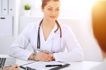 Brunette female doctor talking to patient at hospital office. Physician says about medical exams results for choosing optimal treatment. Healthcare and medicine concept