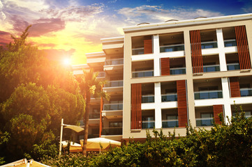 Hotel building with bushes and palm trees against sky with sunset