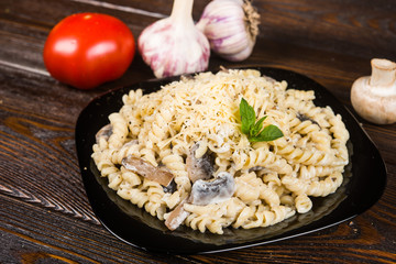 Pasta (spirals pasta)   with mushrooms. Tagliatelle with champignons in creamy sauce  on a black plate on a dark wooden background