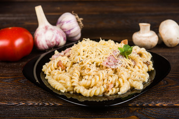 Pasta with ham and chicken on a black plate on a dark wooden background (spirals pasta)