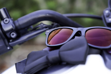 Sunglasses with red glasses and a bow tie lie on a motorcycle