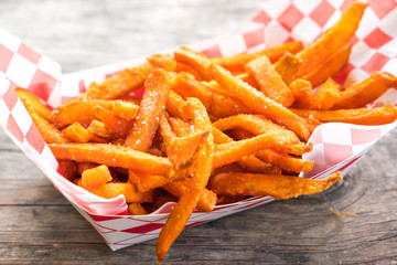 Paper basket of sweet potato fries with salt on rustic wooden table