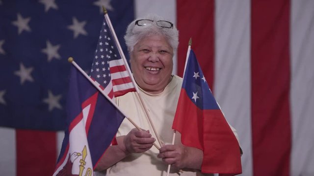 Woman holding Flag of Samoa, American Samoa Flag, and American Flag as she stands in front of American Flag.