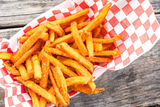 Paper basket of sweet potato fries with salt on rustic wooden table