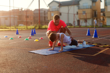 Determinative young football coach learning little boy how to do push ups. Early summer morning...