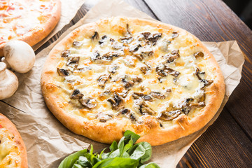 Small mini pizza (mini, miniature) on baking paper on a dark wooden background