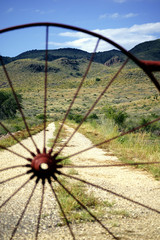 Looking through spokes of a wagon at dirt road leading to open range and mountains  west texas