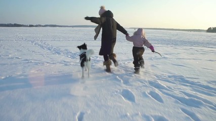Winter fun snow vacation. Young woman with little girl and dog running on the ice of the frozen sea, lake in sunny day in Scandinavia. Slow motion - Powered by Adobe