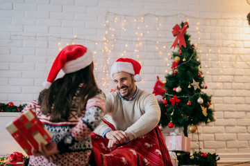 Presents time ! Young happy couple sharing new years presents while sitting on floor covered with...