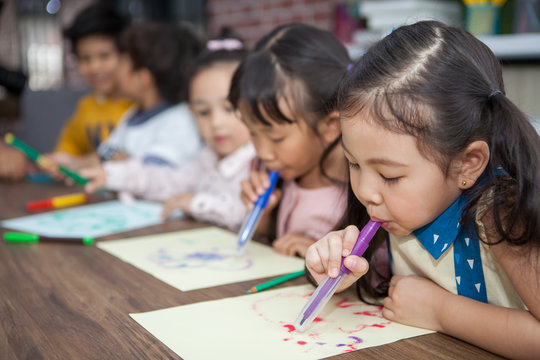 group of Cute little girl and boy student blowing color pen painting  together with nursery teacher in classroom school . Happy children in a kindergarten . kid artist multiethnic