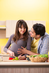Man and pregnant woman preparing salad in kitchen 