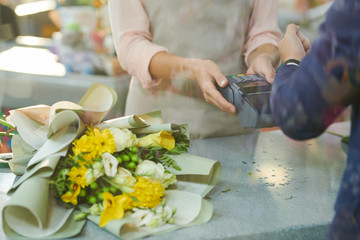 Close up of modern gentleman paying via smartwatch while buying flowers in flower shop, copy space