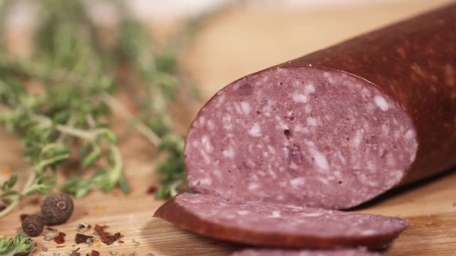 Delicious red meat kielbasa on wooden cutting board next to green herbs at kitchen, close up