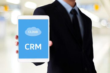 Businessman hand holding digital tablet with CRM, Customer Relationship Management, icon on screen over blur background, success in business concept