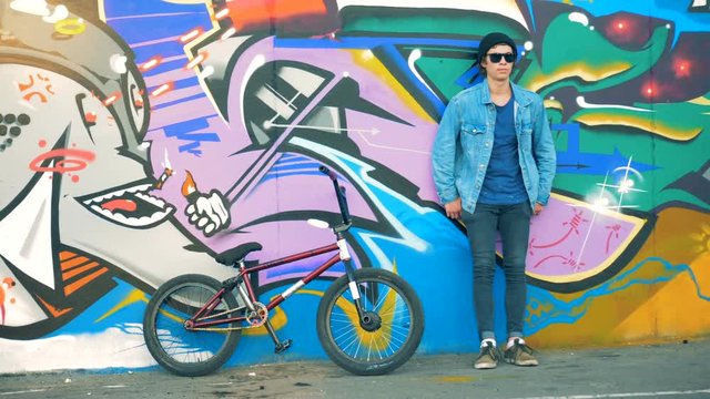 A cyclist leaning on a colored wall. Young stylish Caucasian male teenager.