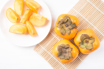 Sliced persimmon fruit on white dish ready for eating, top view