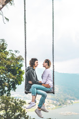 Young honeymoon couple swings in the jungle near the lake, Bali island, Indonesia.