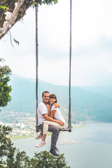 Young honeymoon couple swings in the jungle near the lake, Bali island, Indonesia.