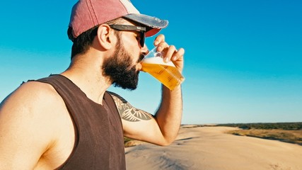 young man enjoying a cup glass of beer outdoor in the desert sand dunes