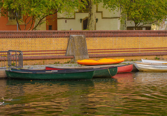 Fototapeta na wymiar bunte Boote liegen an einer Mauer am Ufer, im Hintergrund Häuser und Bäume