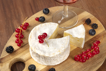 A photo of Camembert cheese with a glass of red wine and fruits, on a dark rustic background with...