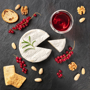 An overhead photo of Camembert cheese with a glass of red wine, fruits and nuts, shot from above on a black background with copy space