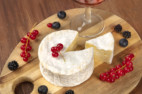 A photo of Camembert cheese with a glass of red wine and fruits, on a dark rustic background with copy space