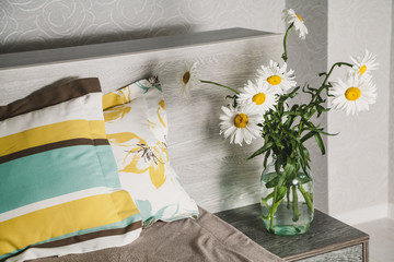 Daisies in vase stand on bedside table before bed
