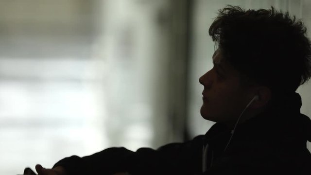 Tennager sitting alone in dark school hallway in front of his locker with headphones in his ears.