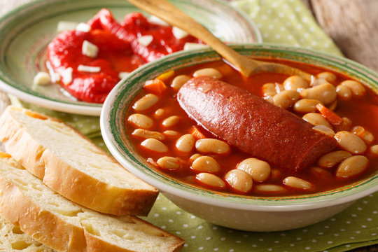 Pasulj (grah) bean soup with sausage is served with bread and bell pepper close-up on a plate. horizontal