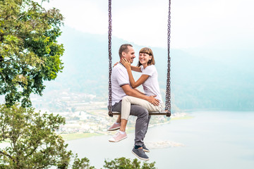 Young honeymoon couple swings in the jungle near the lake, Bali island, Indonesia.