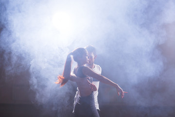 Fototapeta na wymiar Skillful dancers performing in the dark room under the concert light and smoke. Sensual couple performing an artistic and emotional contemporary dance