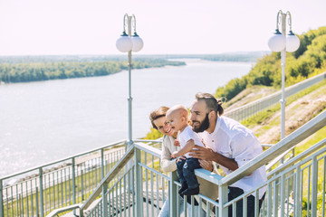 Family mom dad and baby happy with smiles together in the Park walking along the promenade in summer portrait