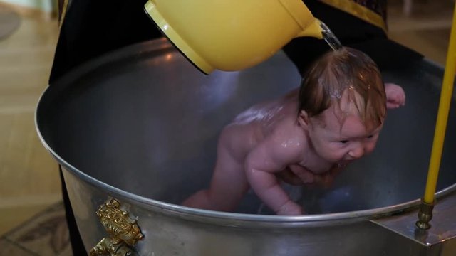 During the infant christening the priest pours baby with holy water