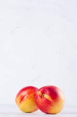 Fresh juicy nectarines on light white wooden board, vertical. Fresh summer season background.