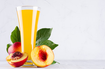 Fresh peach juice in elegance glass  and ripe red nectarines with green leaves  on soft white wood board, closeup. Sweet summer fruits and drinks.