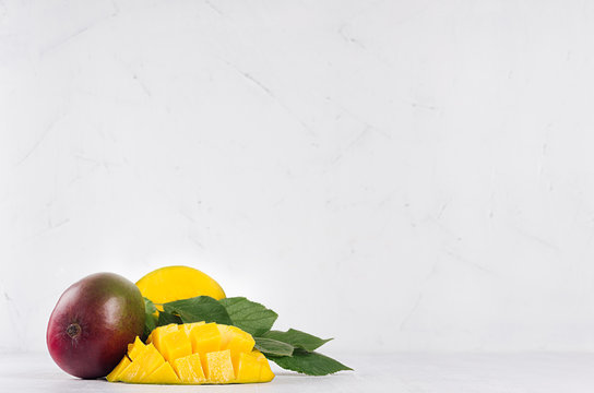 Juicy mango with ripe yellow sliced half and green leaves on soft light white wood background. Elegant moder kitchen interior with tropical fruit.