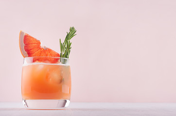 Cocktail de pamplemousse froid décoré de brindilles de romarin et de tranches d& 39 agrumes sur fond rose.