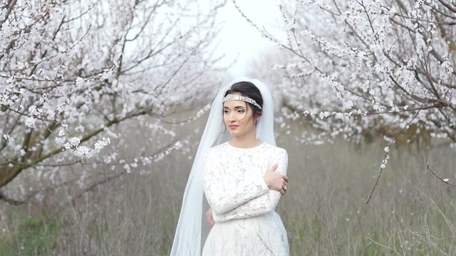 Beautiful brunette bride in white dress posing in blooming tree garden background