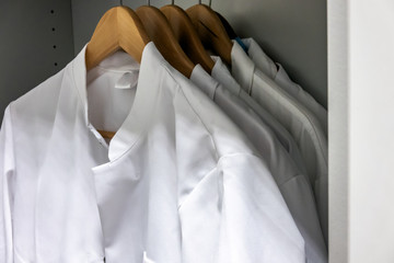 White smocks on wooden hangers hang in the cupboard of a laboratory