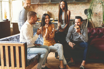 Spending great time with best friends. Group of cheerful young people enjoying food and drinks while spending nice time in cofortable chairs on the kitchen together.